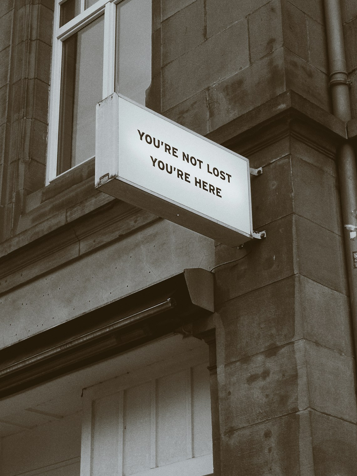 A sign on a street wall reading ‘You’re not lost, you’re here’